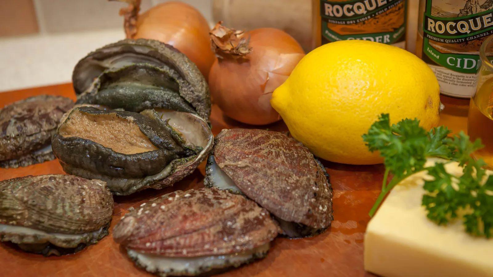 Shellfish on a wooden surface next to a lemon, onions and some butter.