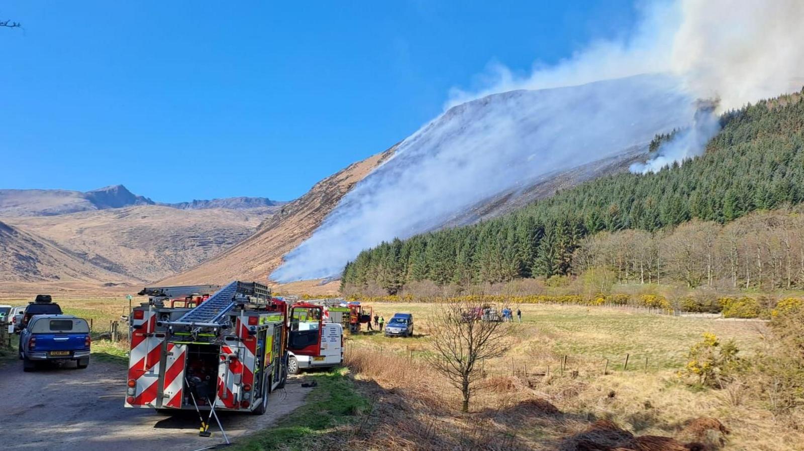 Fire engines parked in front of hills that are covered in smoke.