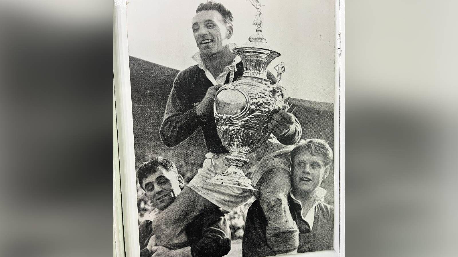 A black-and-white framed photo of two Workington Town players lifting another player holding the Challenge cup.