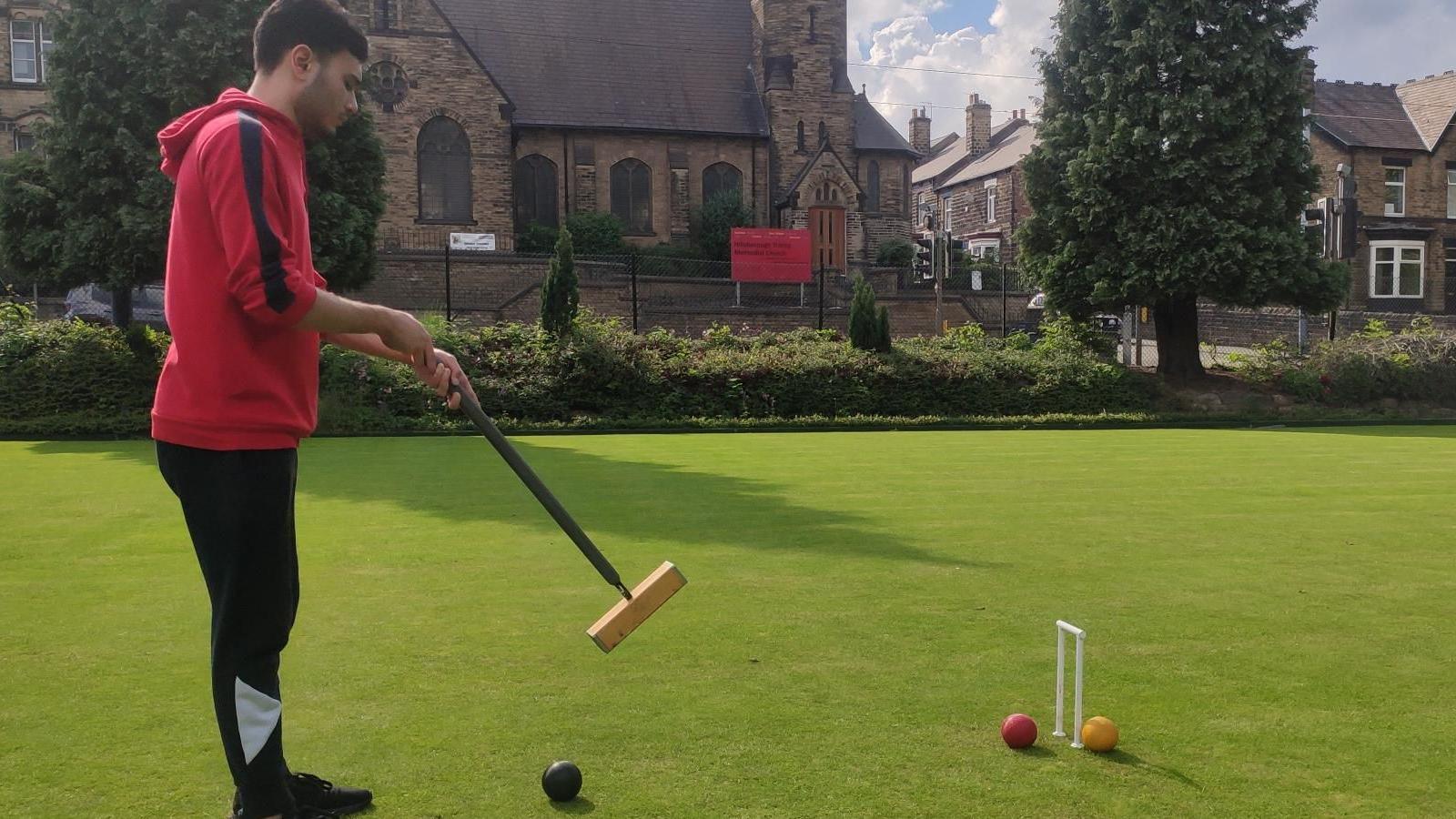 A man in a red hoodie hits a red ball with a mallet