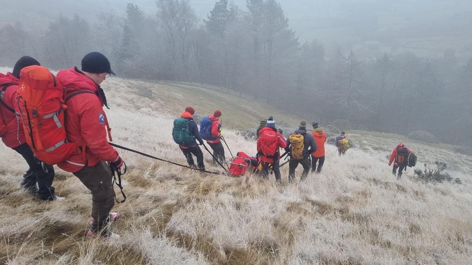 Rescue team members work together with ropes and specialist equipment to move casualty down hill in wintry conditions