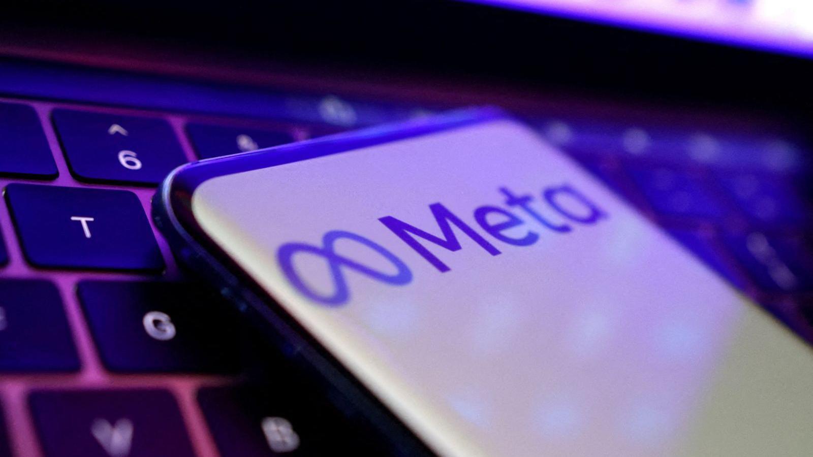A phone placed on a laptop keyboard. The phone shows the infinity sign meta logo and the word meta next to it. Purple on a white background