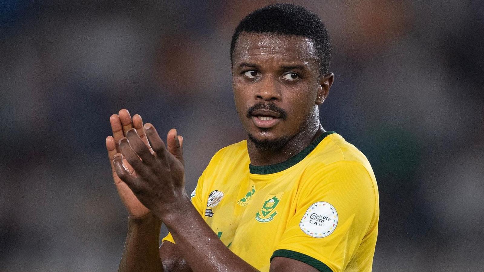 Teboho Mokoena, wearing a yellow South Africa football shirt, holds his hands up as he applauds during a football game