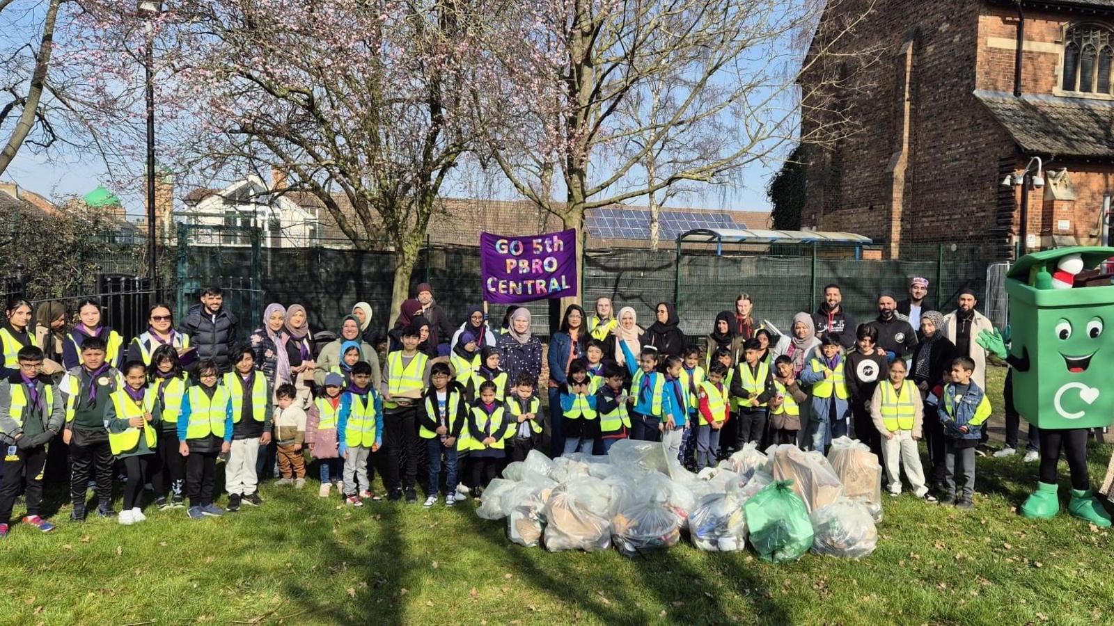 Participants all wearing hi-vis jackets standing in a row, with bags of litter in front.