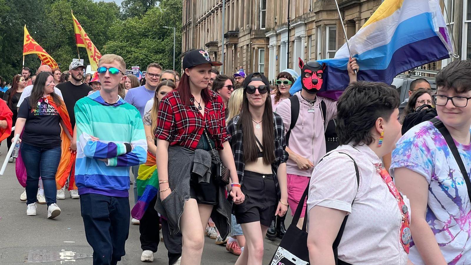 Pride marchers in Glasgow carrying flags and wearing colourful clothes