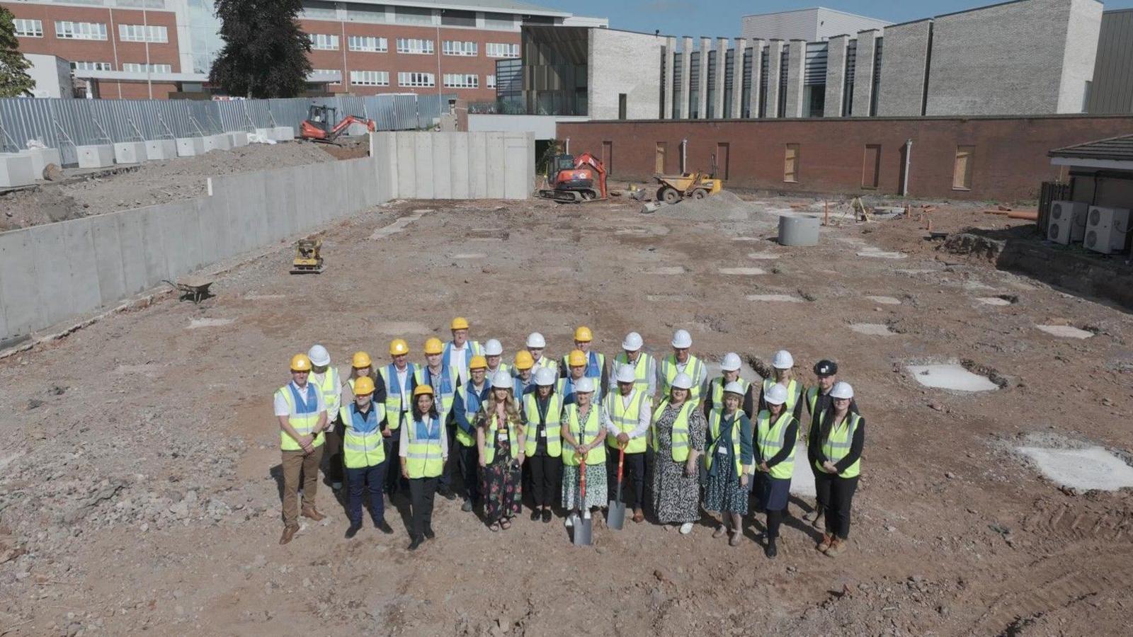 An aerial shot of representatives of the North Cumbria Integrated Care Trust wearing hi-vis vests and holding spades on the site where the new unit will be built.