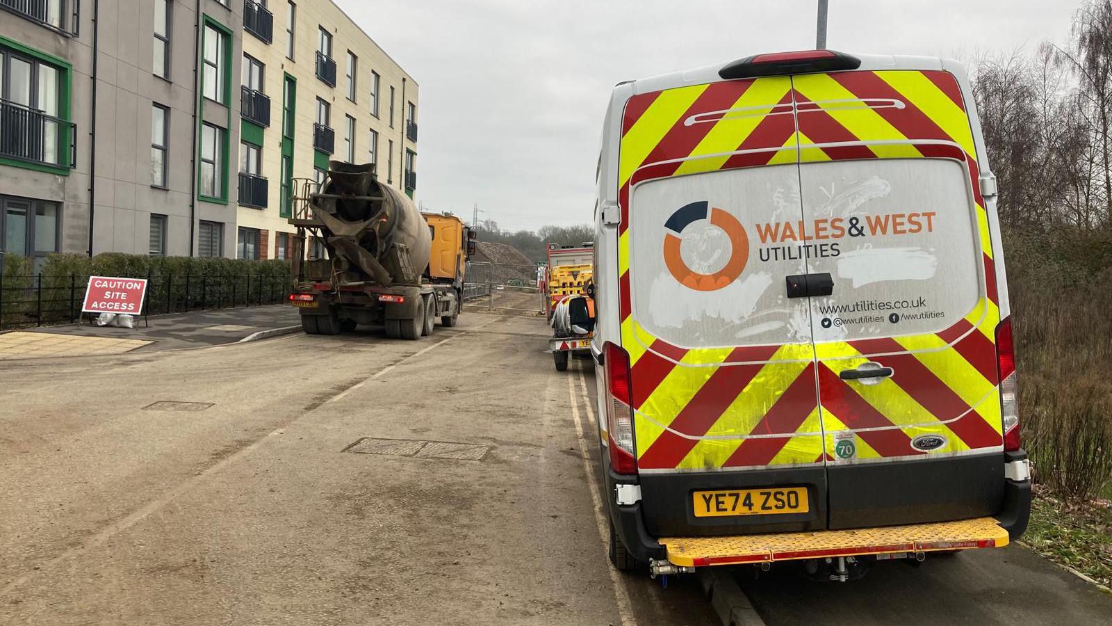 A Wales & West Utilities van parked up at the site of the incident. Construction vehicles are also visible along the road, and a building site in the distance alongside a hotel. 