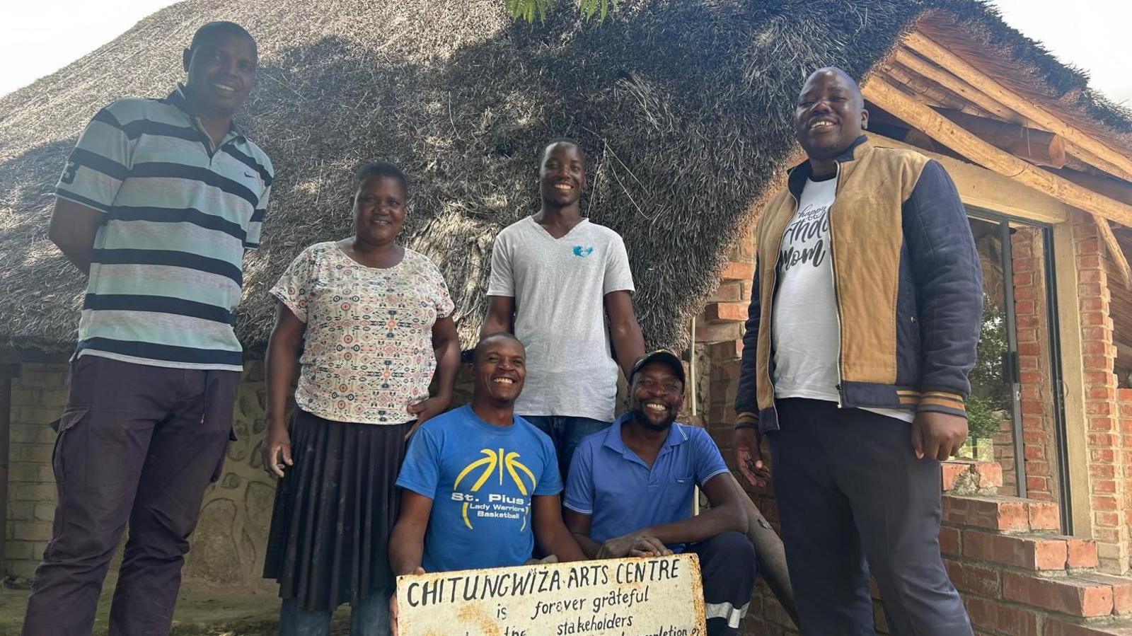 CAC Committee members at the launch of the competition, outside their arts centre. It is a brick building with a thatched roof.