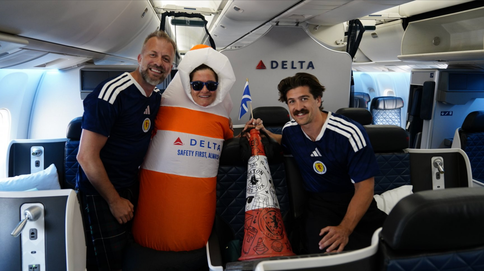 Andrew Dobbie is wearing a Scotland football shirt. He is seen with a member of the Delta cabin crew dressed as a cone, as well as the cone and Danny Campbell, also wearing a Scotland shirt.