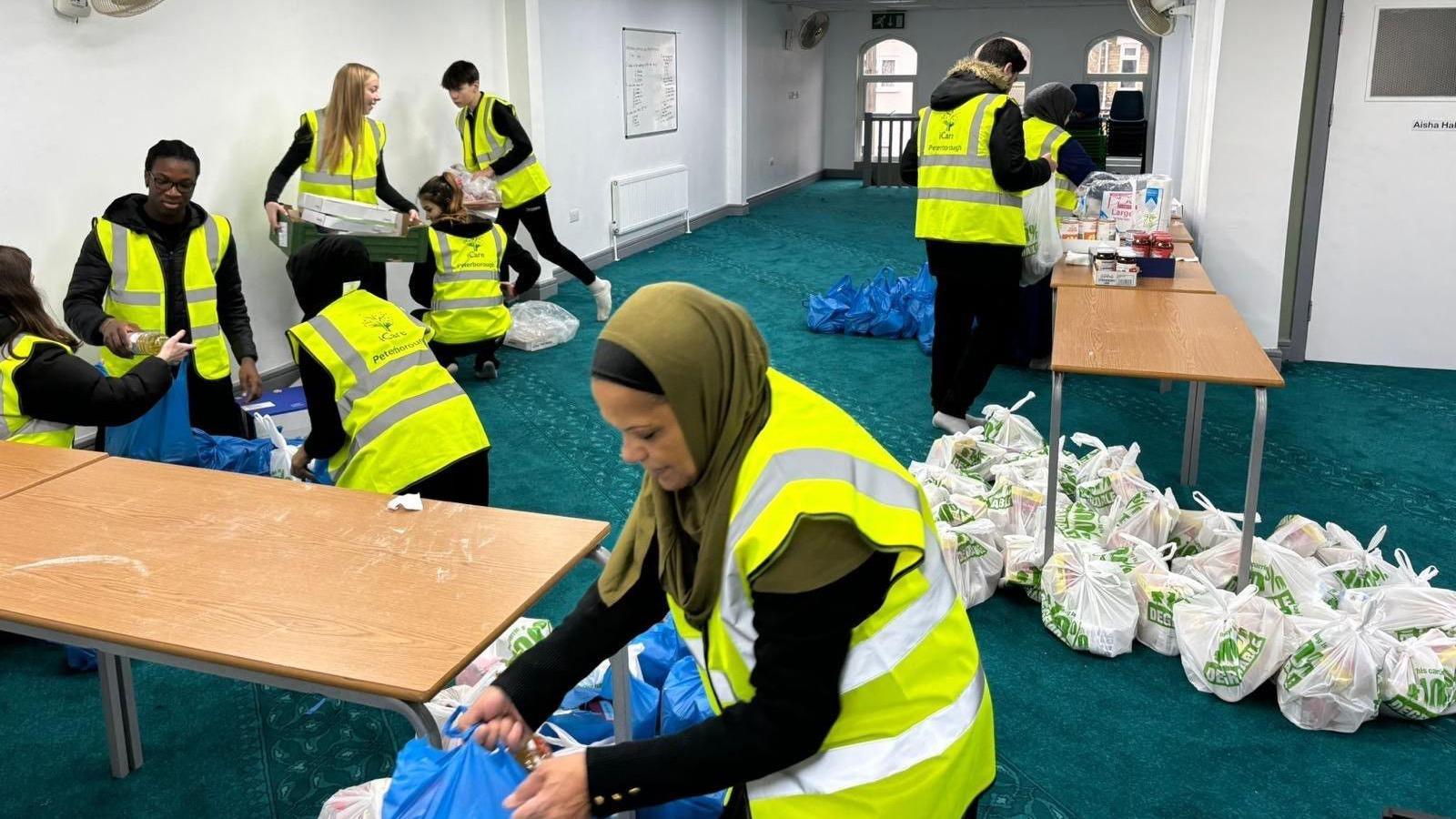 Volunteers wearing green high-visibility jackets- packing food parcels at a room inside the Mosque