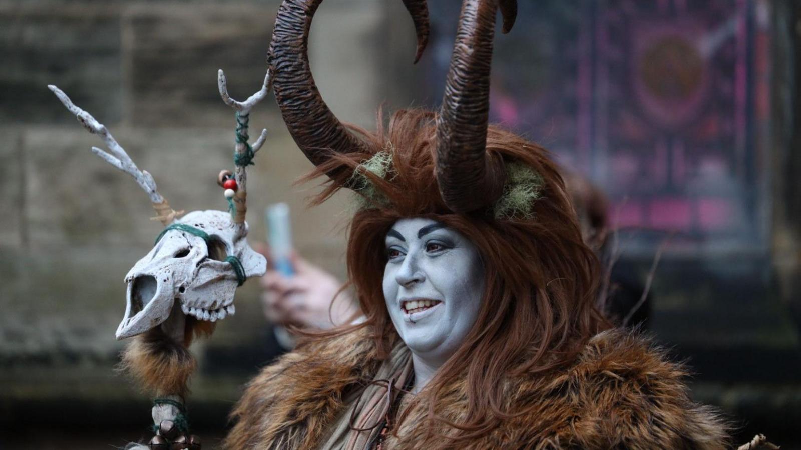 A woman dressed as Krampus in brown fur with horns and face paints, and holding a skull 