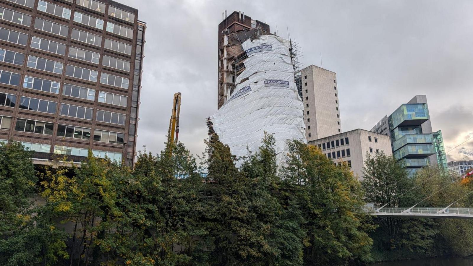 white scaffolding wrap slides down high -rise building with trees in front and other buildings around