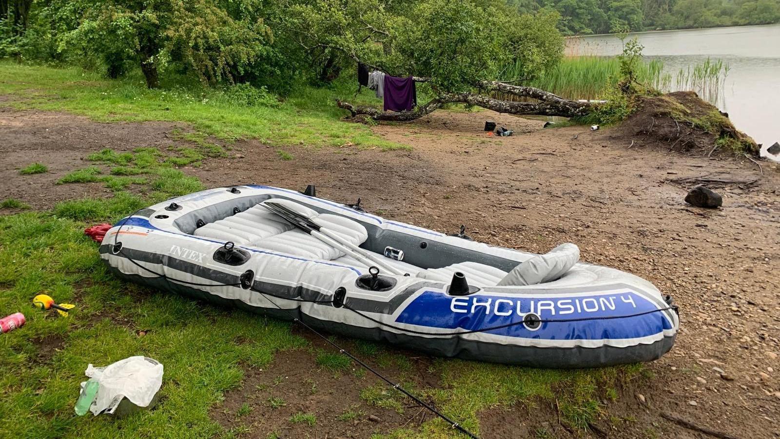 An inflatable boat with the words Excursion 4 lies beside rubbish on the edge of a loch