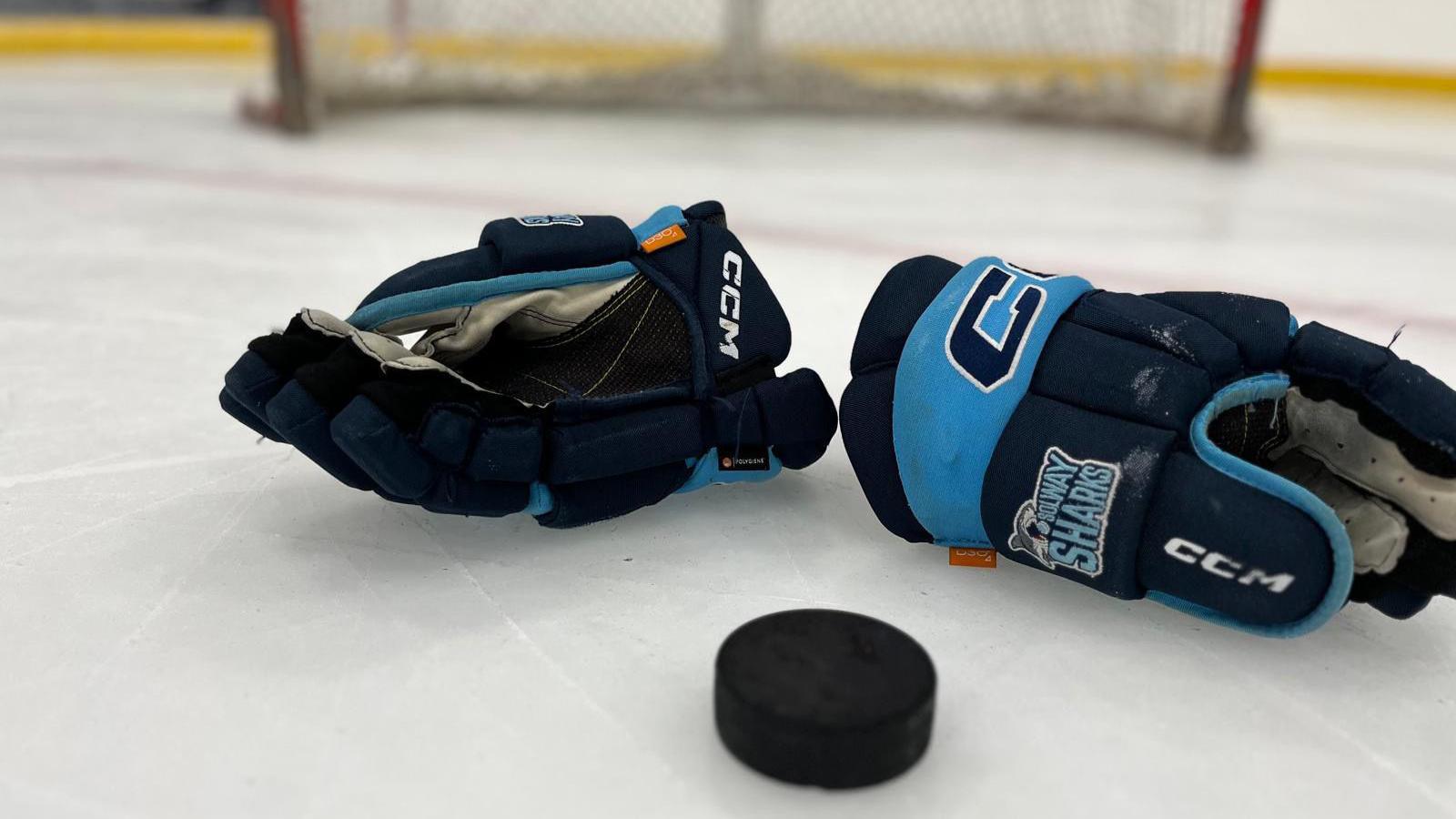 Two big Solway Sharks ice hockey gloves around a puck on ice