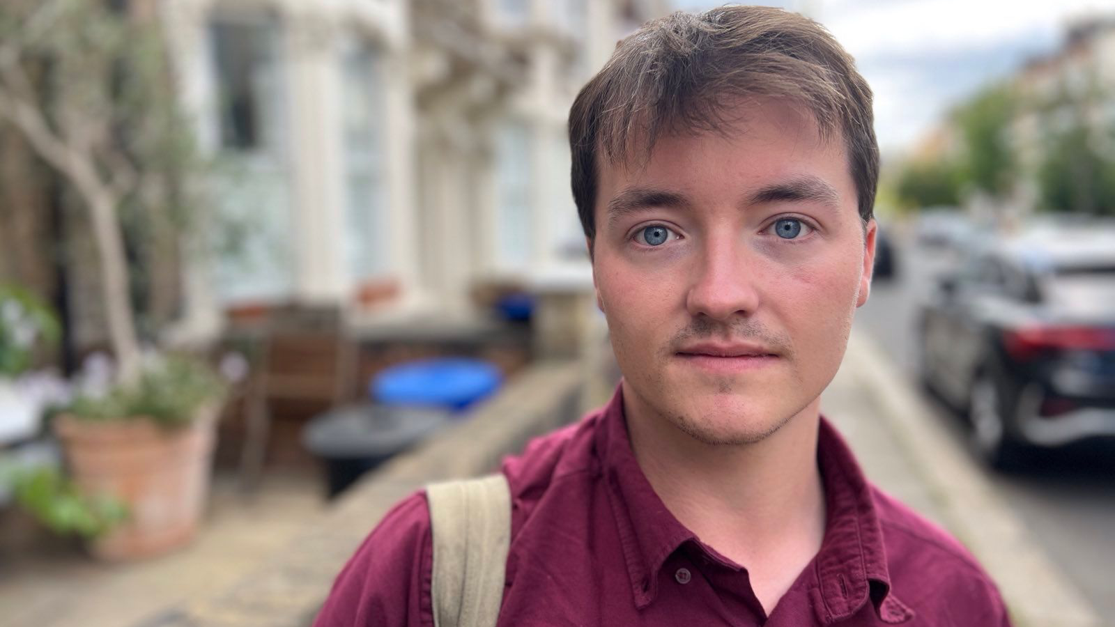 A young man with a rucksack is pictured hunting for home on a street of terraced houses and parked cars.