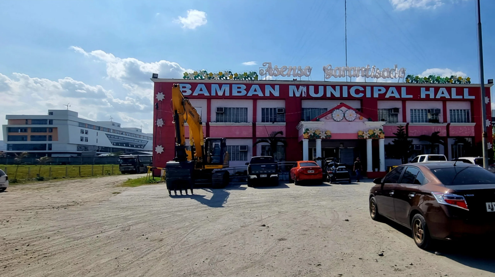 A squat building two floors tall, painted red and pink and decorated with flowers, with the words "Bamban Municipal Hall" emblazoned across the top of its facade in large silver letters