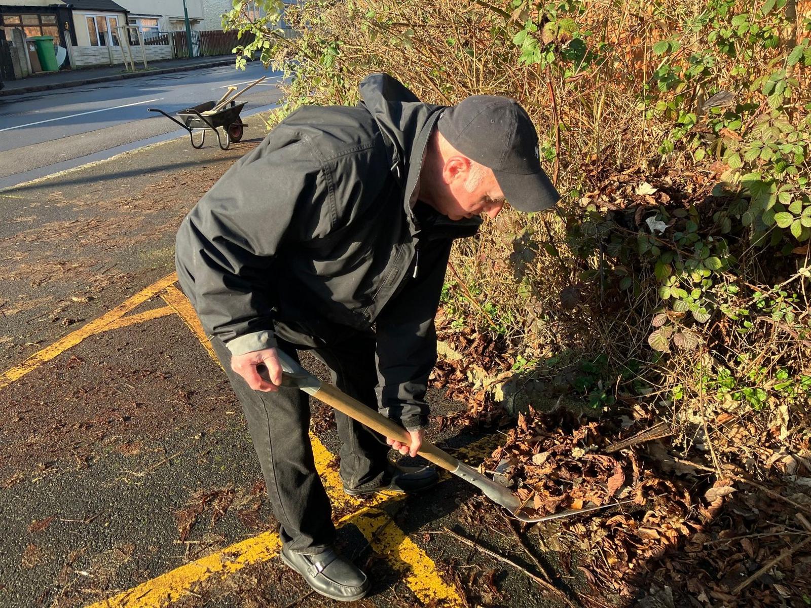 A man using a spade to clear leaf litter from a pavement