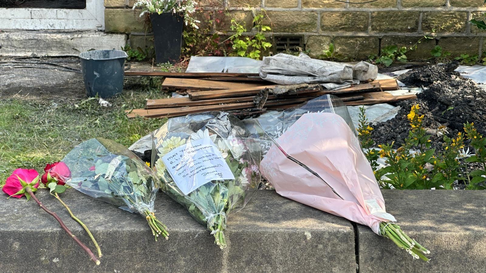 Three bunches of flower left on a wall outside a house damaged by fire 