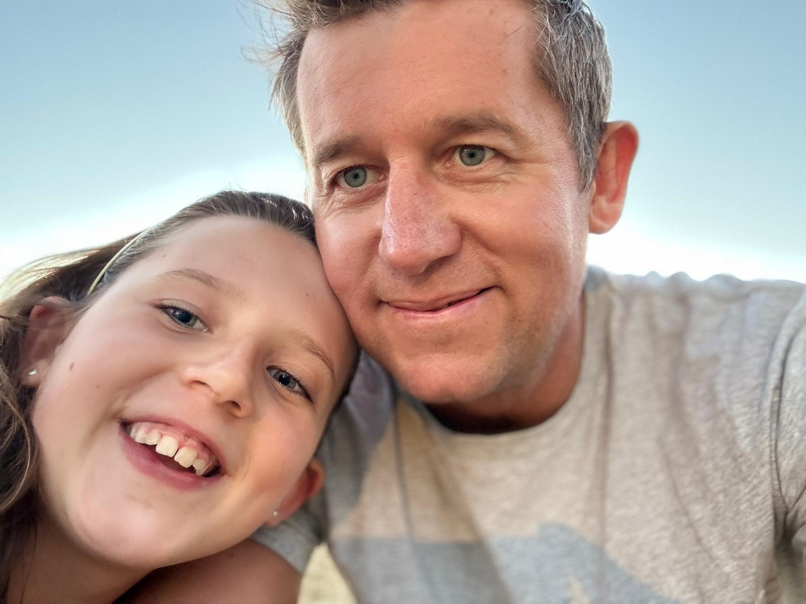 A man and a young girl are leaning into each other while they smile into the camera. 