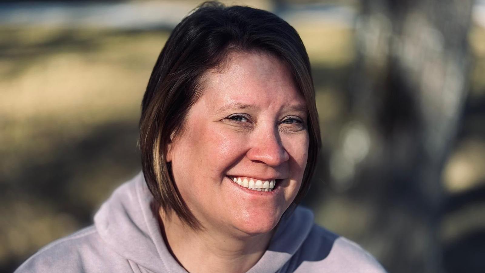 Caroline Turner-Inskip smiles at the camera, wearing a grey hoodie. She has short dark hair.