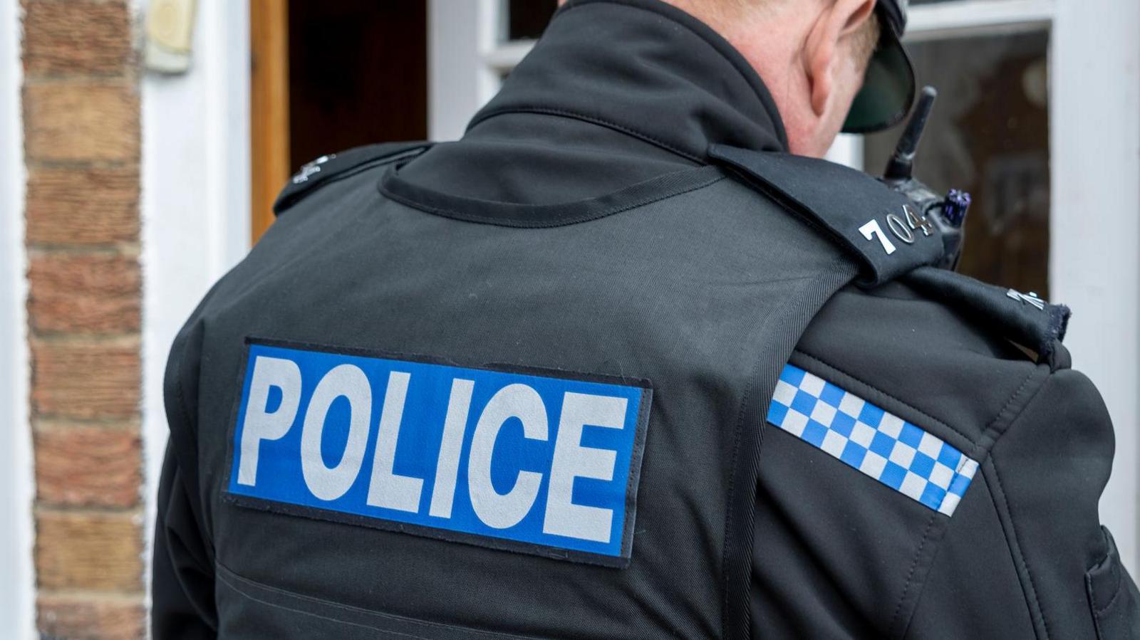 The back of a policeman outside a property.