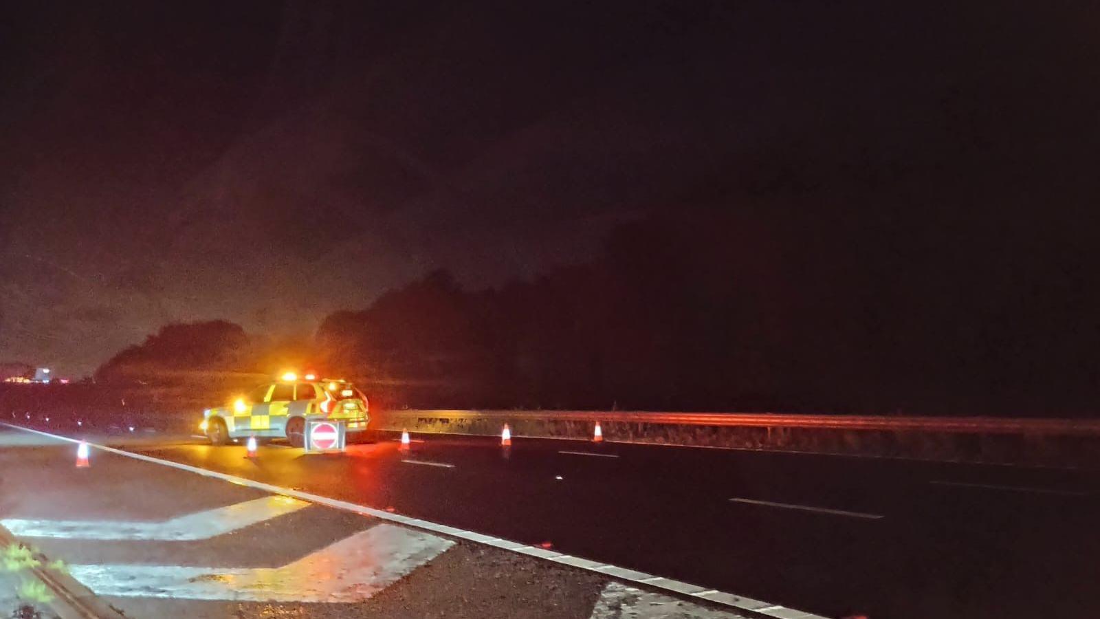 Police car on the M5 southbound near Junction 14. Traffic cones can be seen by the car, as well as a road closed sign. The police car has its lights on. 