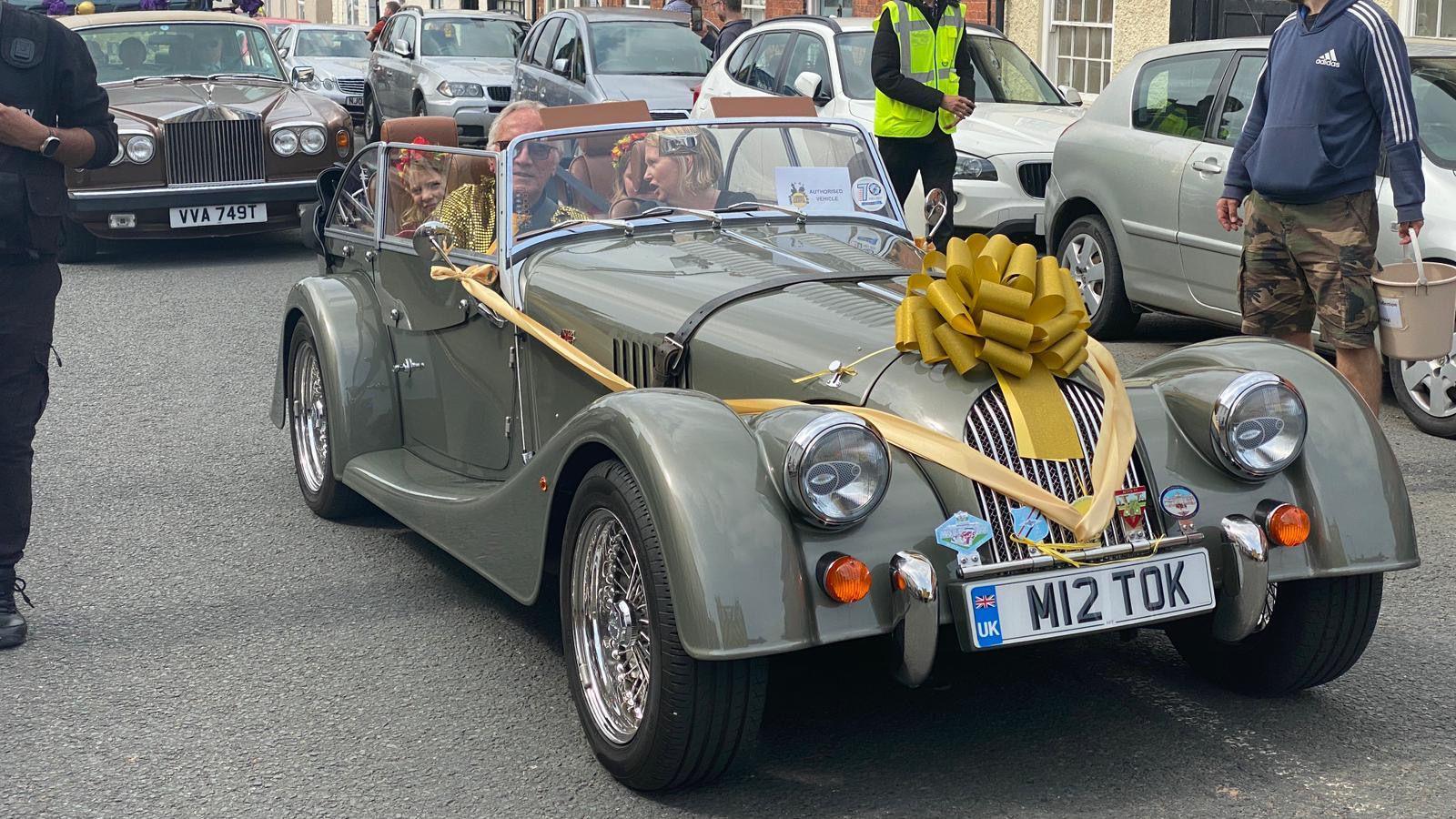 A grey car decorated with a large gold rosette for the carnival