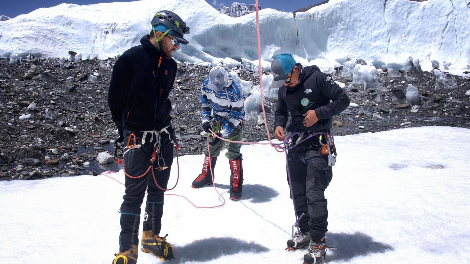 Three men attached to one another with ropes, standing on a snowy plain