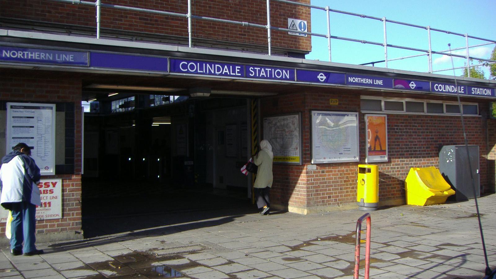 Colindale station exterior shows blue signage and passengers entering. There are two yellow bins outside, one for salt