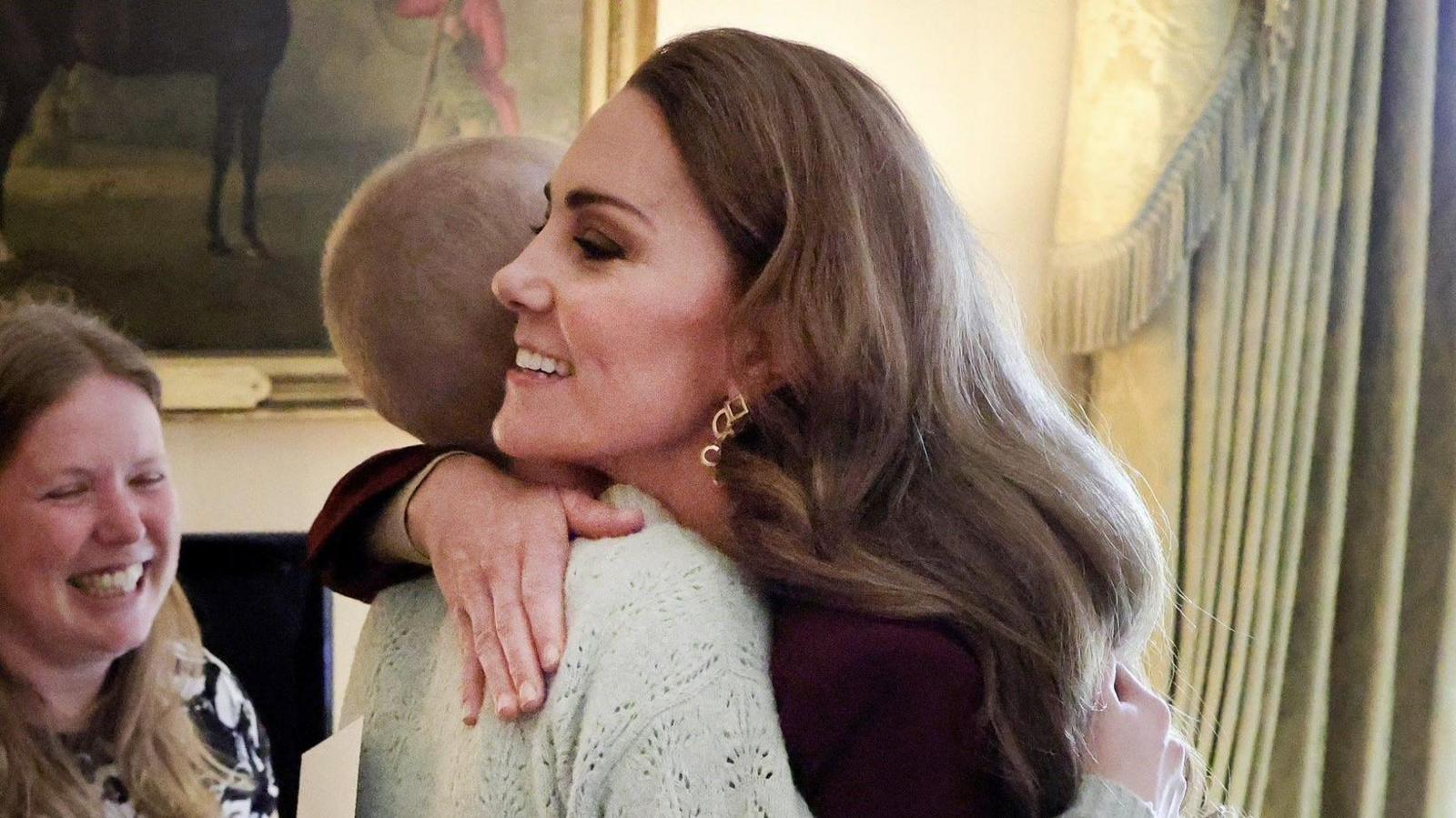 Liz on the left is wearing a pale green jumper seen embracing the Princess of Wales who is wearing a purple dress, long brown hair and a gold earring shown