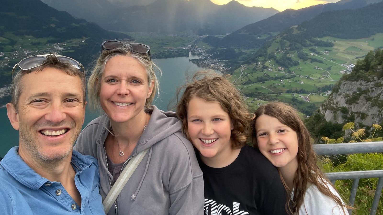 A selfie photo of Amy, Arlo, Flo and Neil with a mountainous landscape and a lake behind them.