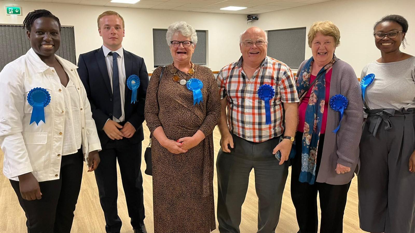 A group of politicians in a line, wearing smart clothing, and smiling for the picture after a by-election.