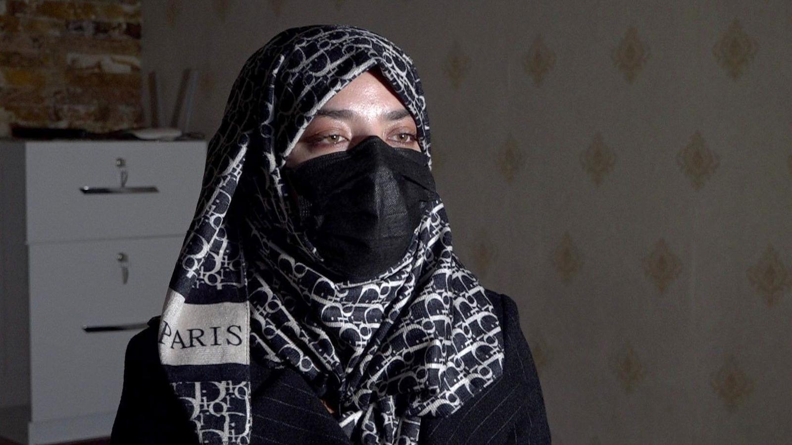 A woman wearing a headscarf and face mask sits in front of the camera