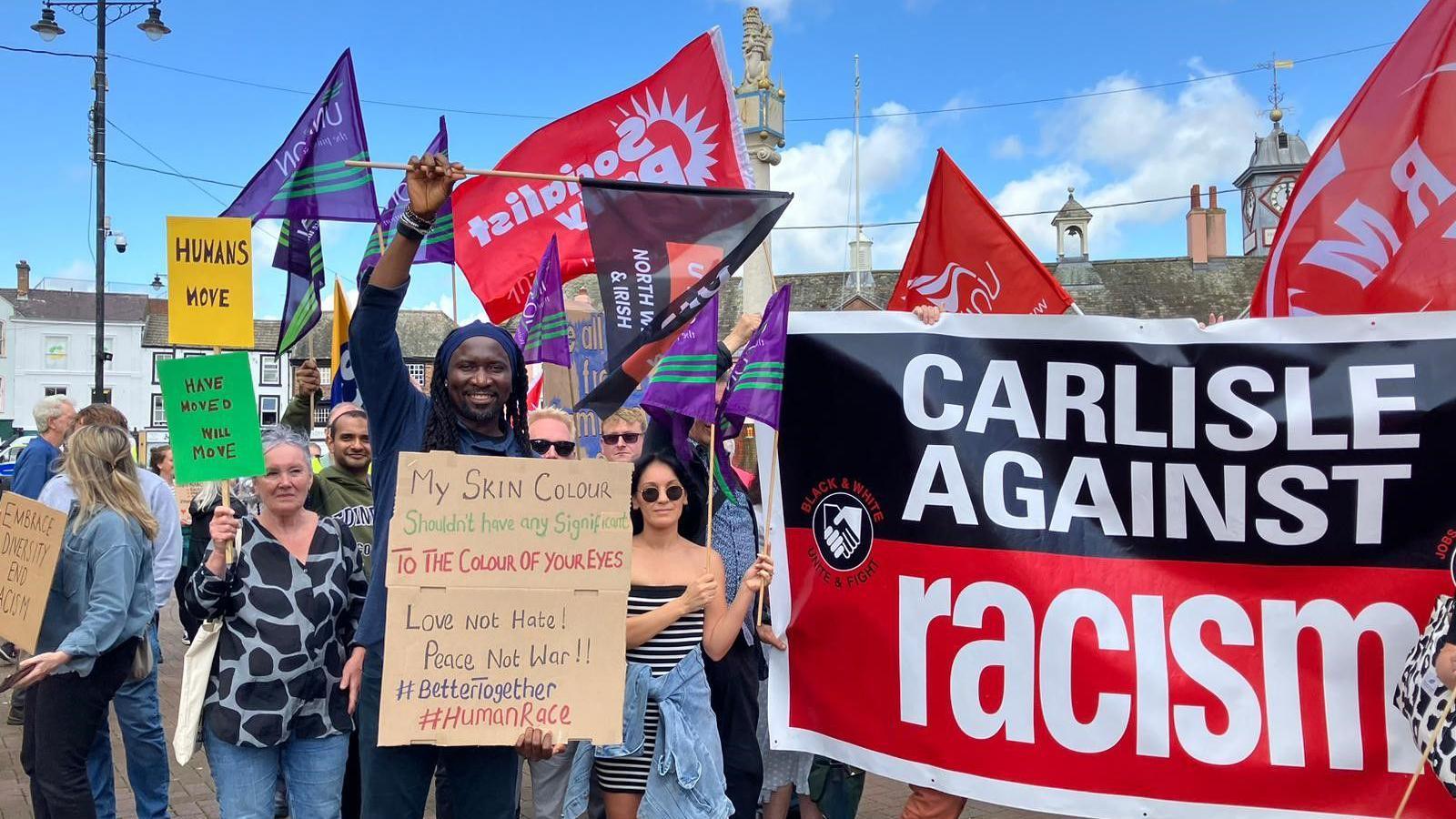 Kelvin Enabulele displays a hand-written anti-racism banner as he stands alongside other people at the event in Carlisle