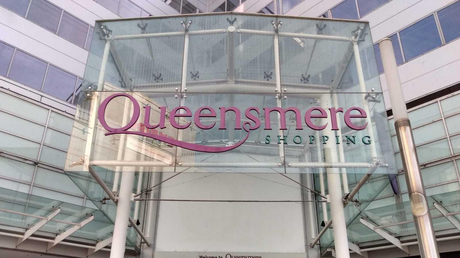 A glass sign above a set of double doors saying "Queensmere shopping" in pink and green writing.