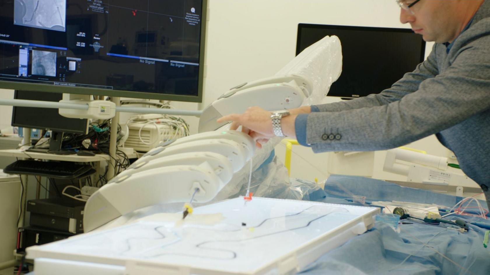 A man touching the wires of a robot that carries out a thrombectomy.