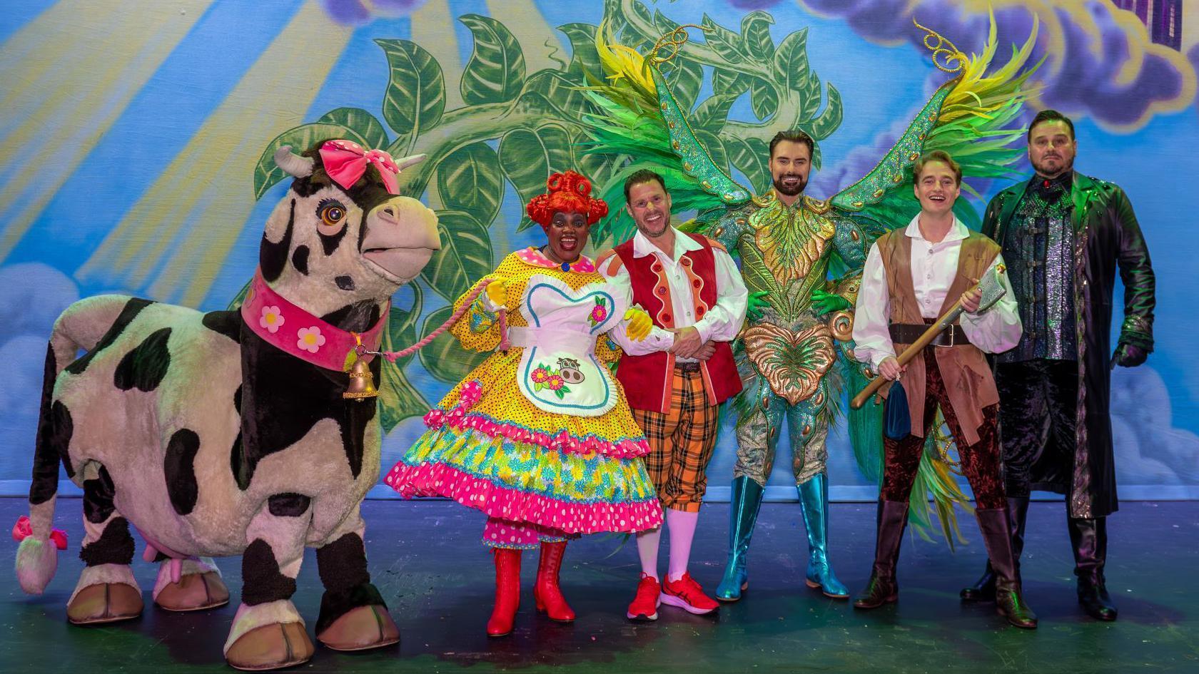 Rylan Clark on stage with fellow pantomime actors, all in various extravagant costumes.