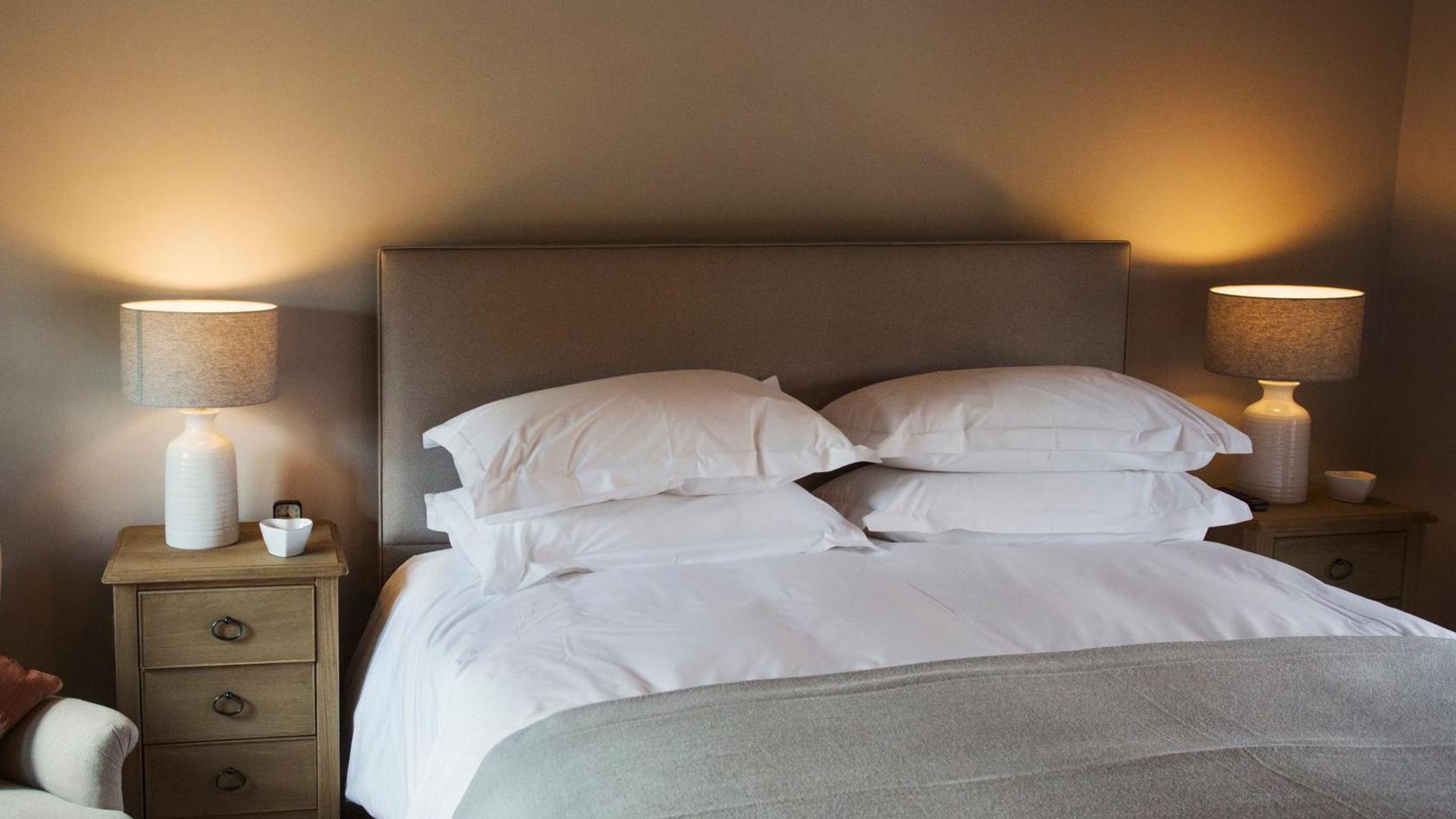 A hotel room showing a double bed with big pillows and beige decor