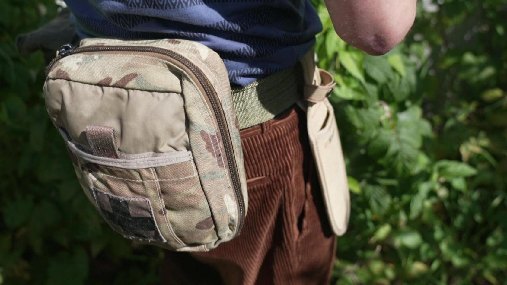 Image shows Mr Rowe's midriff, around which he has fastened a khaki-coloured utility belt which includes a small pouch and a sheath for the trowel.