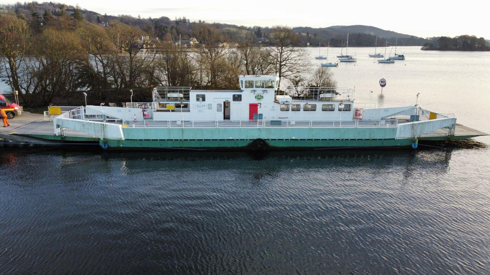 The Windermere ferry moored at Windermere. It has no passengers visible. There are sailing boats in the background.