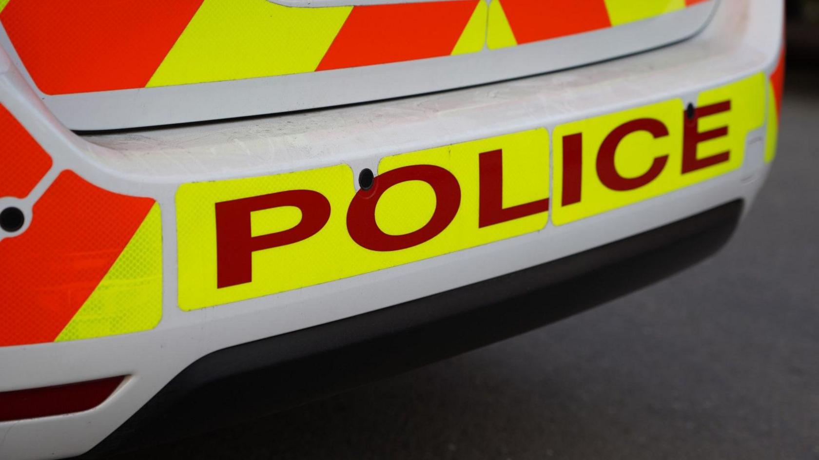 Rear of a liveried police car with the word "police" written in large capital letters in red on a yellow background