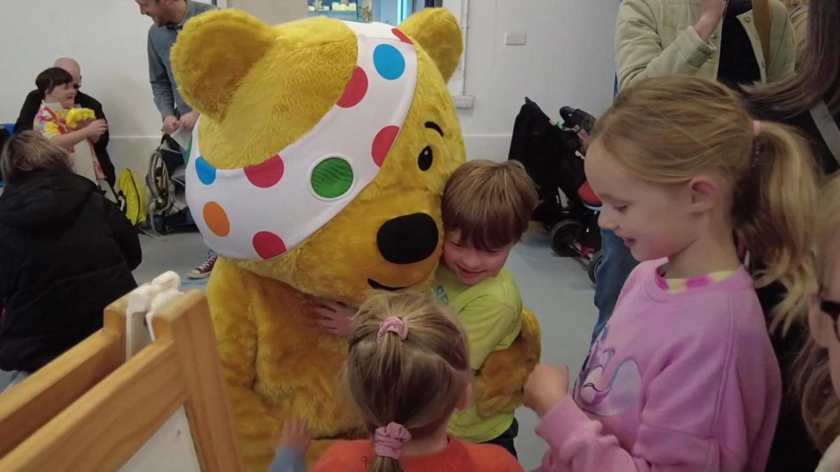 BBC Children In Need Pudsey the bear hugging two children at the charity centre