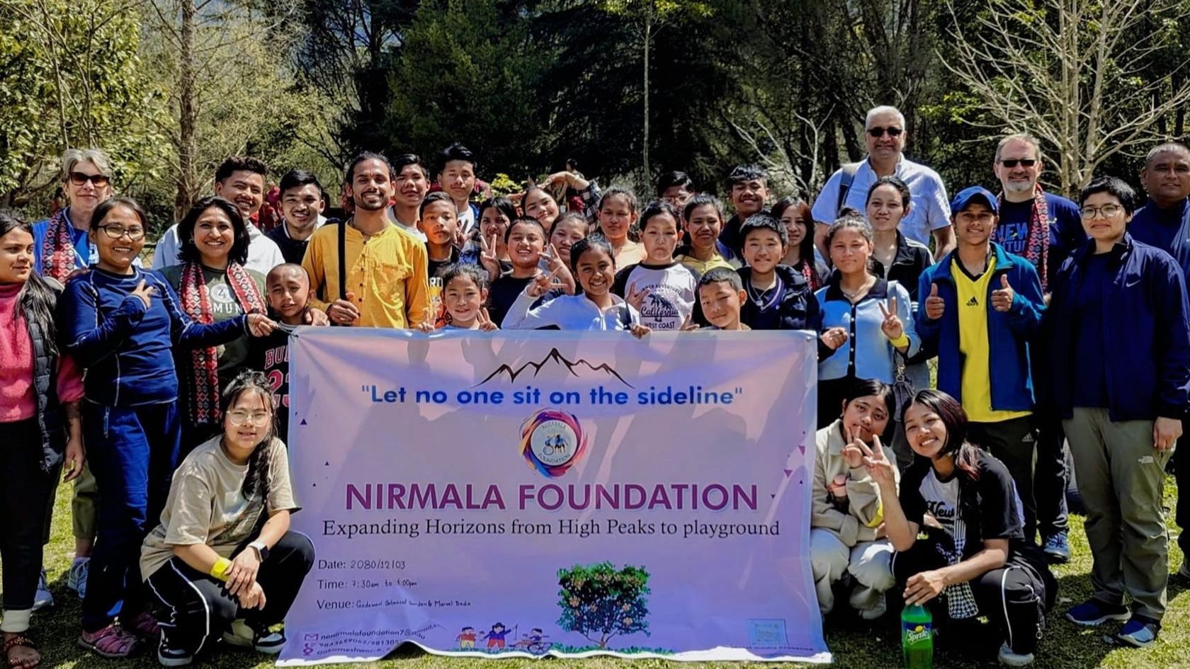 A group of 34 people, many of them children, with a pink flag promoting the Nirmala Foundation in Nepal