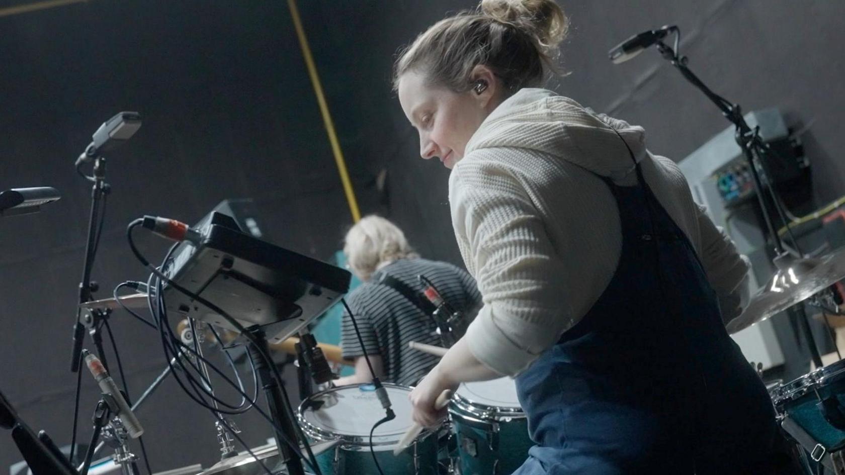 Janette playing drums in a rehearsal room with the band.