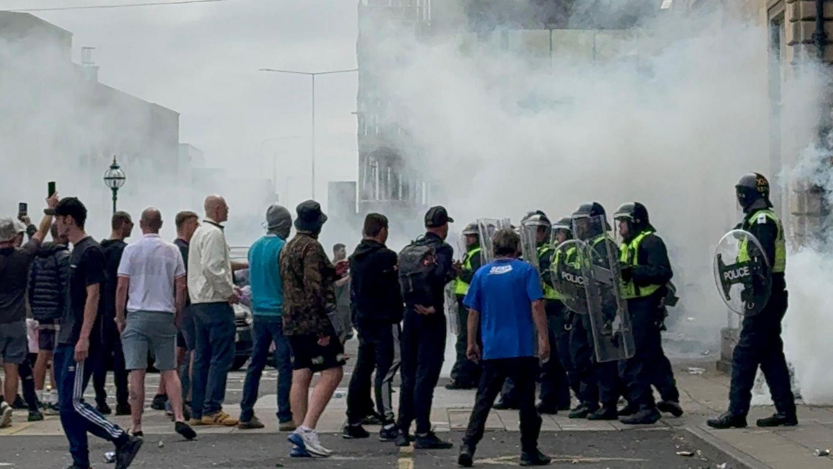 Crowd of people in front of a line of police officers in riot gear