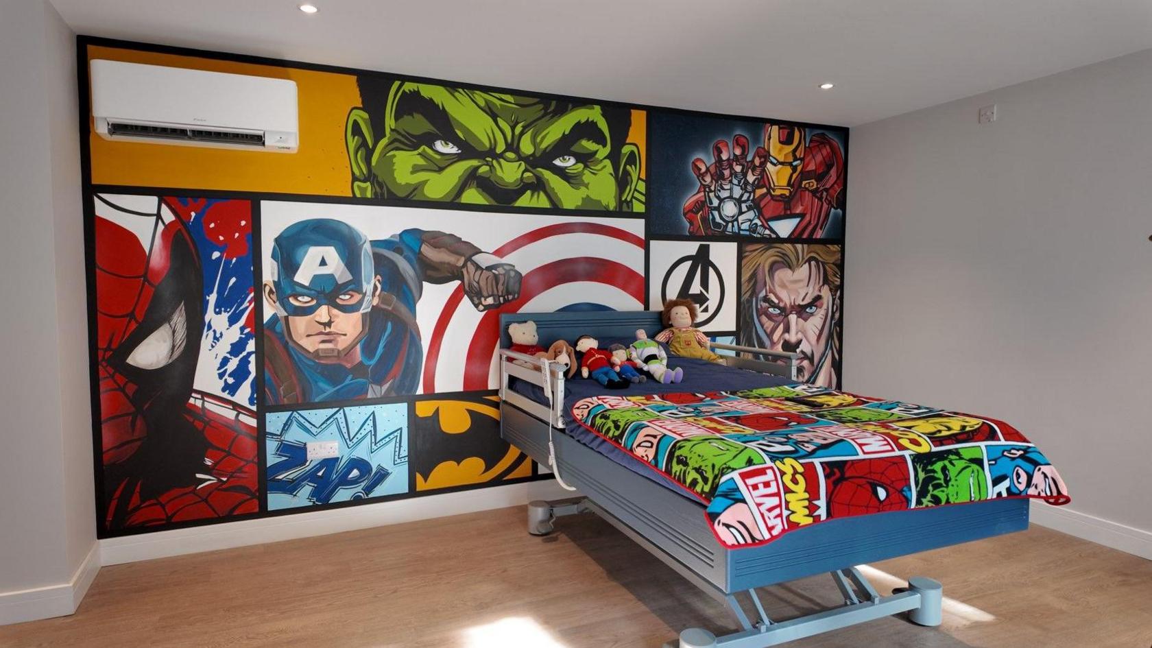 A child's bedroom with a special bed for medical needs is decorated with super hero imagery in a comic book style.