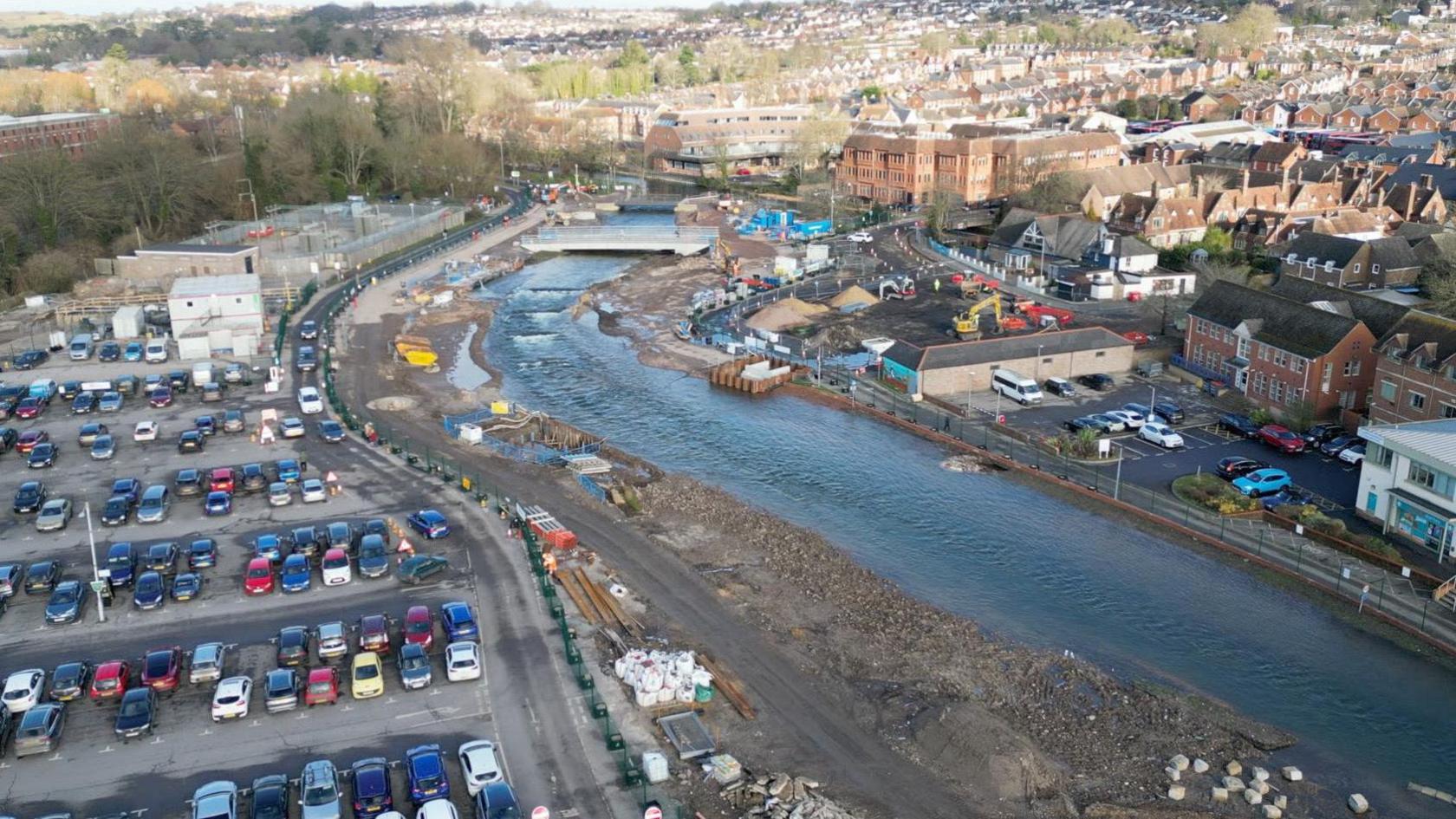 A drone shot of the river park scheme in the centre of Salisbury. A large car park is on the left of the image with the River Avon running through the image on the right. The Salisbury skyline is in the background.