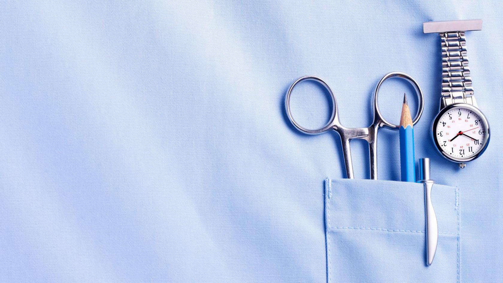 A stock image of a nurse's top pocket with a watch, pair of scissors, pencil and pen in the pocket.