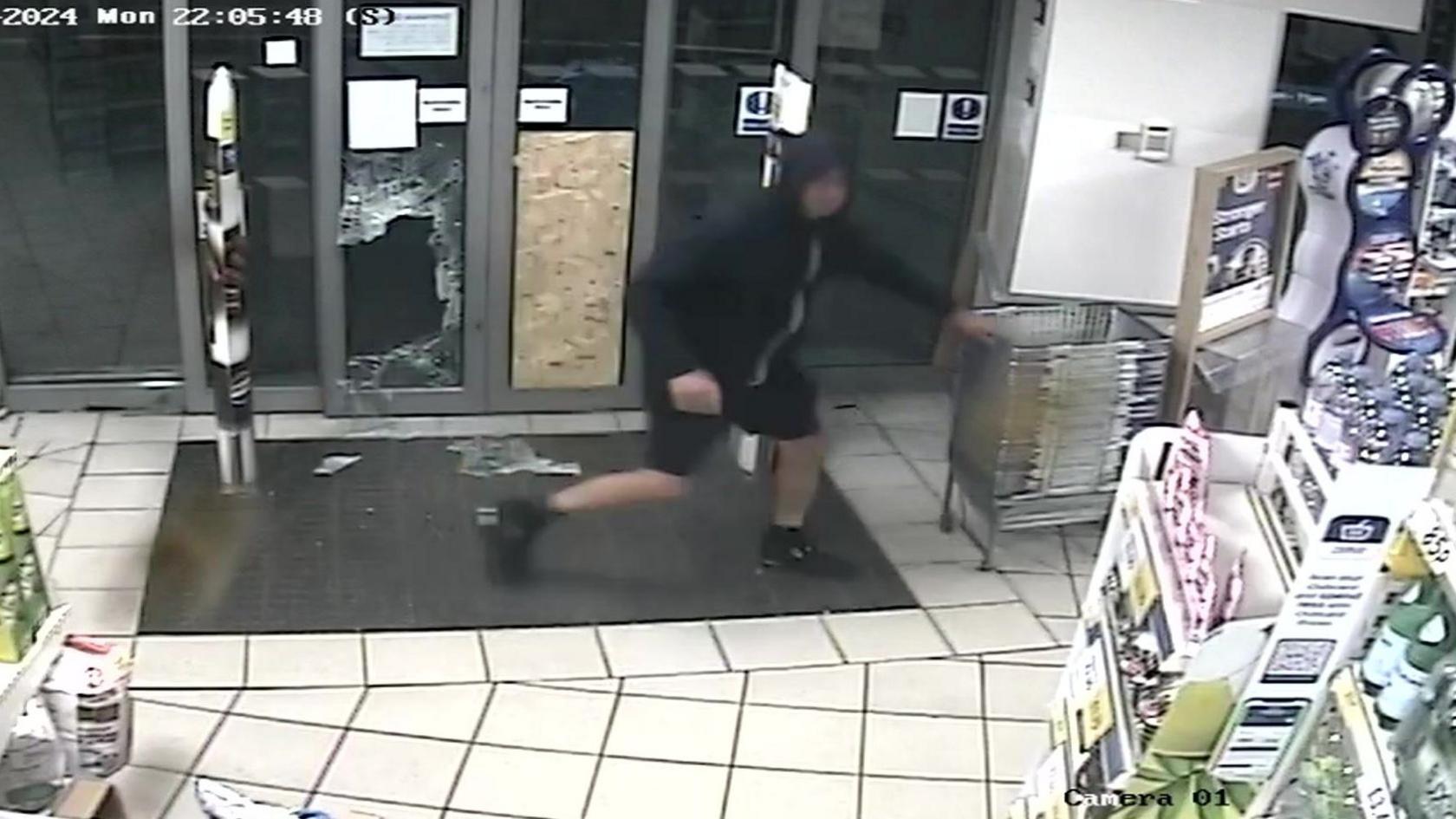 A man is seen on CCTV going to collect a shopping basket with a broken door window in the background