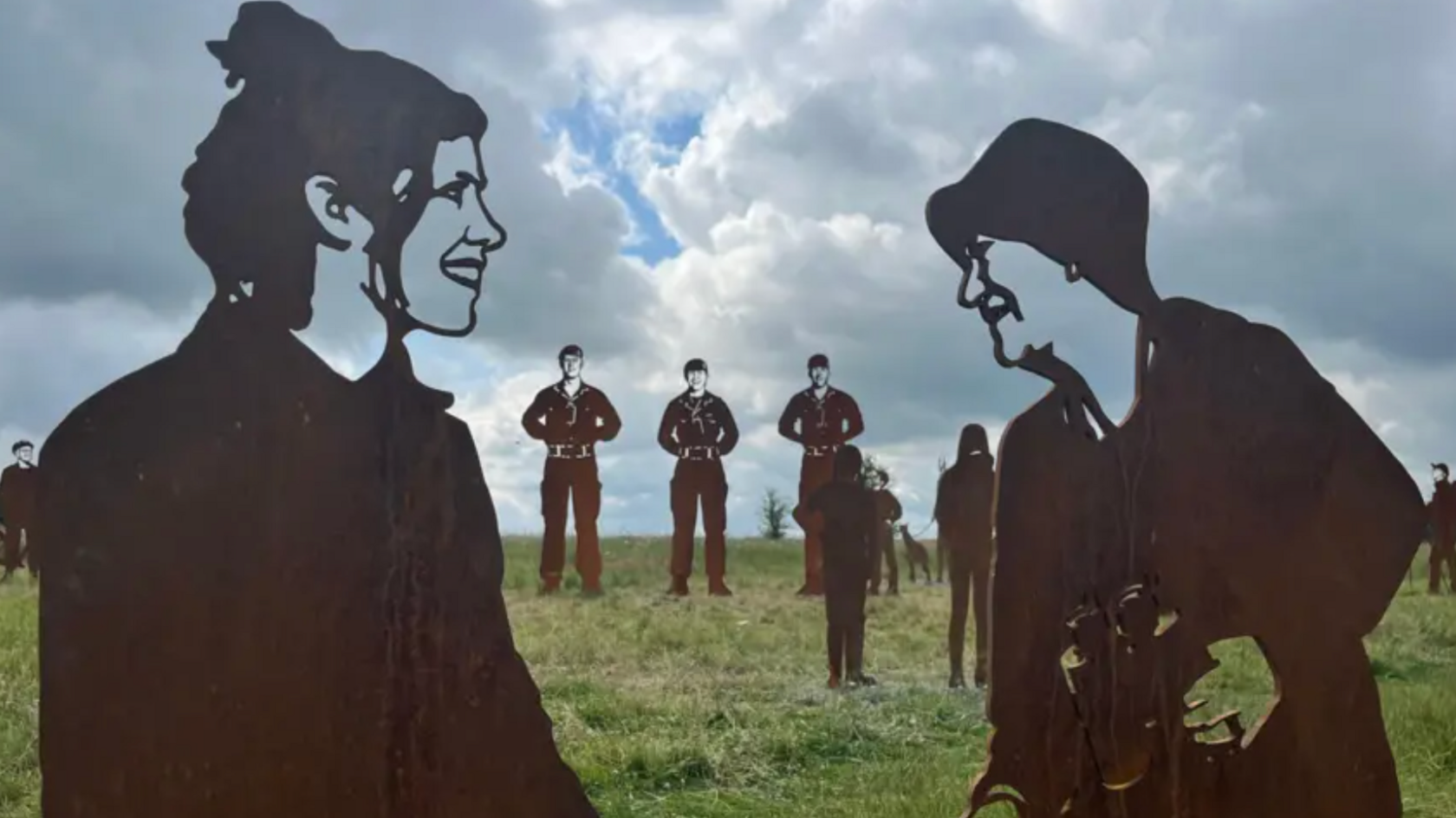 The statues of military personnel on military land in Salisbury. Centre there are two female figures staring at one another. On the left, the statue of a woman has her hair up and is smiling looking at a female figure on the right. The right hand figure is holding a pair of binoculars. 